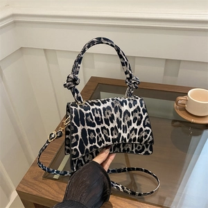 Leopard print handbag with curved base and knotted handle on a minimalist wooden table