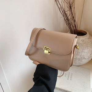 Minimalist beige leather crossbody bag with a gold square clasp held by a model