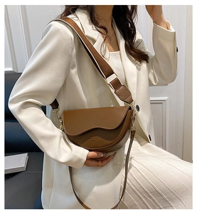 Close-up of brown leather saddle bag with wide woven strap and contrast stitching detail