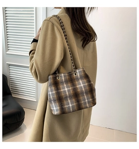 Detail of plaid wool bucket bag with gold chain strap on a camel-colored coat