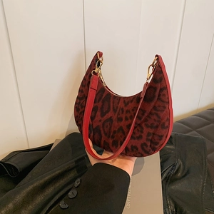 Fashionable leopard print crescent bag in dark red suede held by hand with shoulder strap