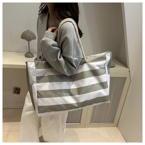Detail of striped canvas tote bag with thick woven rope handles shown on a model