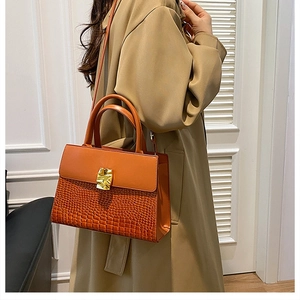 Detail of tan crocodile pattern handbag with gold clasp on khaki trench coat background