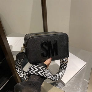 Chic black camera bag with SM logo, wide geometric shoulder strap and gold hardware