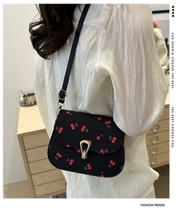 Détail d'un sac besace noir à imprimé cerises avec boucle en métal et bandoulière