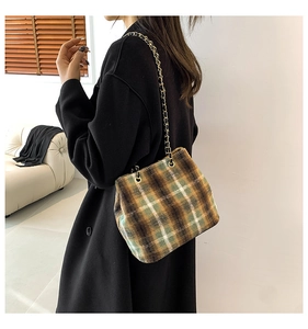 Detail of wool blend plaid bucket bag with gold chain strap on a black coat