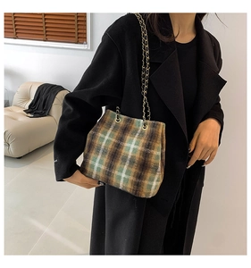 Detail of vintage plaid wool tote bag with golden chain straps against a black coat