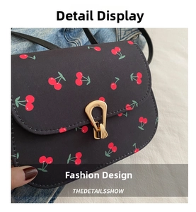 Detailed view of black saddle bag with cherry print and golden horseshoe metal buckle