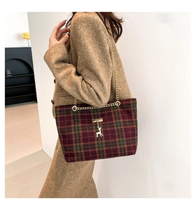 Detail of red and green plaid tote bag with golden deer charm and chain strap
