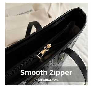 Detail view of smooth golden zipper and black quilted texture on leather tote bag