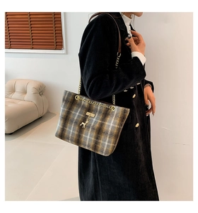 Detailed view of plaid wool tote bag with gold chain strap and deer charm on a black coat