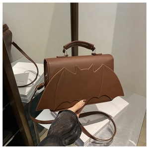 Détail d'un sac bandoulière marron foncé en forme de chauve-souris avec rabat à ailes