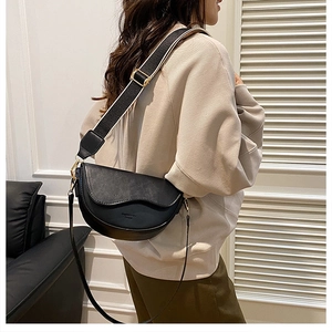 Detail of black saddle bag with striped canvas wide strap and matte finish on beige sweater