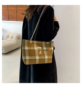 Detail of checkered woolen tote bag with gold deer pendant and chain strap on shoulder