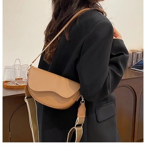 Close-up of a tan saddle bag with a wavy flap and wide striped textile shoulder strap
