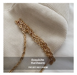 Macro view of a polished gold metal chain strap on an off-white textured knit fabric