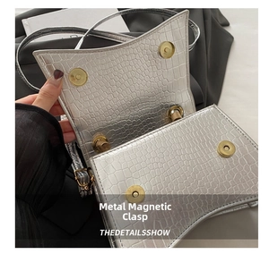 Detail of silver crocodile-embossed bag featuring dual magnetic metal buckles on the flap