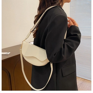 Detail of a creamy white saddle bag featuring unique wavy flap design and long strap