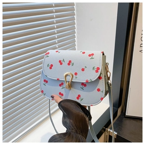 Détail du sac selle bleu clair à imprimé cerises avec boucle dorée et texture en cuir PU