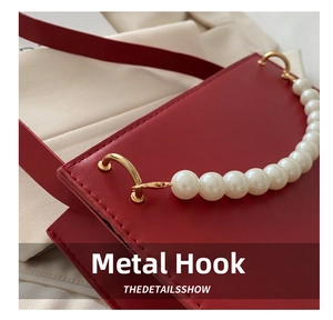 Detail of red leather bag showing golden hook hardware and pearl beaded handle decoration
