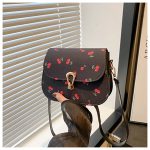 Gros plan du sac besace noir avec imprimé cerises et boucle dorée en forme de U