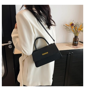 Detail of black lychee grain leather handbag with gold Fashion text on white blazer