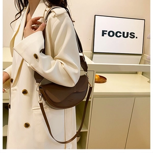 Detailed view of a brown vintage saddle bag with gold hardware on a white coat