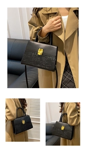 Detail view of the black textured crocodile pattern leather and gold metal buckle on the bag
