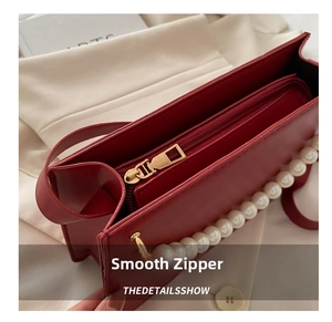 Detail of red leather tote bag showing smooth gold zipper closure and pearl decoration