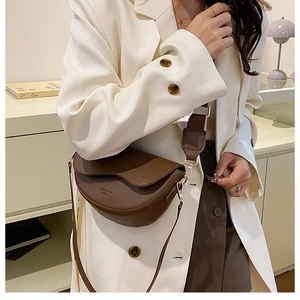 Detailed view of a dark brown half-moon saddle bag with a wide adjustable strap on a model