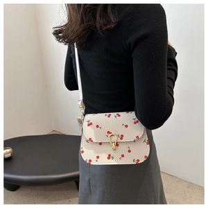 Modèle portant un sac selle blanc à imprimé cerises avec boucle métallique dorée en U