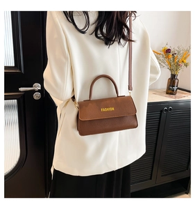 Close-up of caramel litchi textured crossbody bag with FASHION lettering on a white suit