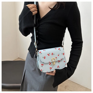 Detail of light blue saddle bag with red cherry print and golden U-shaped metal lock