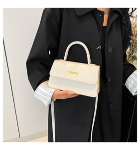 Detail of off-white leather handbag showing letter print and contrast black coat outfit