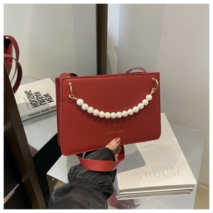 Detailed close-up of a red matte leather handbag featuring an elegant pearl chain ornament