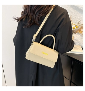 Detail view of beige textured leather crossbody bag with Fashion lettering and strap