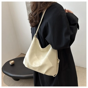Detail of off-white embossed tote bag with ZSKE logo worn over a black winter coat