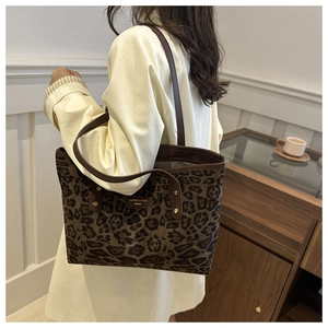 Detail of leopard print tote bag featuring brown leather straps and metallic logo plaque