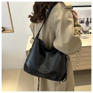 Minimalist large black leather tote bag shown on a model wearing a khaki trench coat