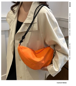 Detail of bright orange half-moon crossbody bag with black knotted rope shoulder strap