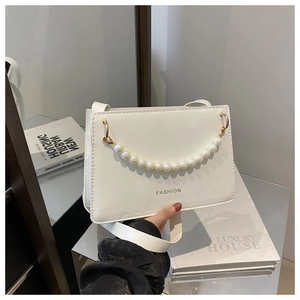 Close-up of white minimalist handbag with gold FASHION text and elegant pearl handle