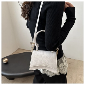 Detail of white crocodile pattern PU leather handbag with gold hardware and curved base
