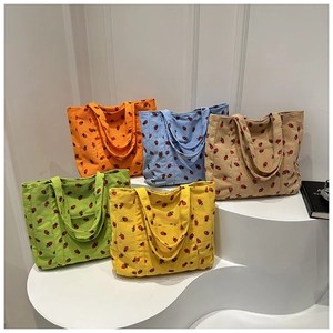 Detail of corduroy tote bags showing strawberry patterns and fabric textures in five colors
