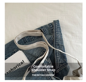 Detail of blue denim bucket bag featuring a wide white shoulder strap and metal buckle