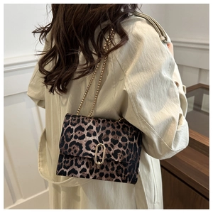 Detailed view of a leopard print flap bag with gold chain strap on a trench coat