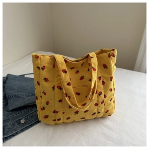 Close-up of yellow corduroy tote bag with red strawberry prints and front pocket detail