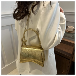 Detail of gold hourglass shoulder bag with crocodile texture on a white suit model