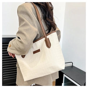 Detail of minimalist tote bag with textured surface and brown leather trim on woman
