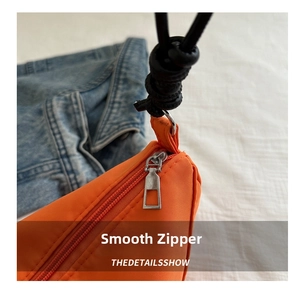 Detail of smooth metal zipper on orange oxford nylon crossbody bag with black cord