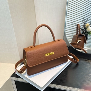 Brown lychee leather tote bag with FASHION text and golden hardware on white books